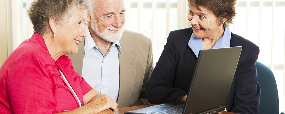 Three older people in a group looking at a laptop