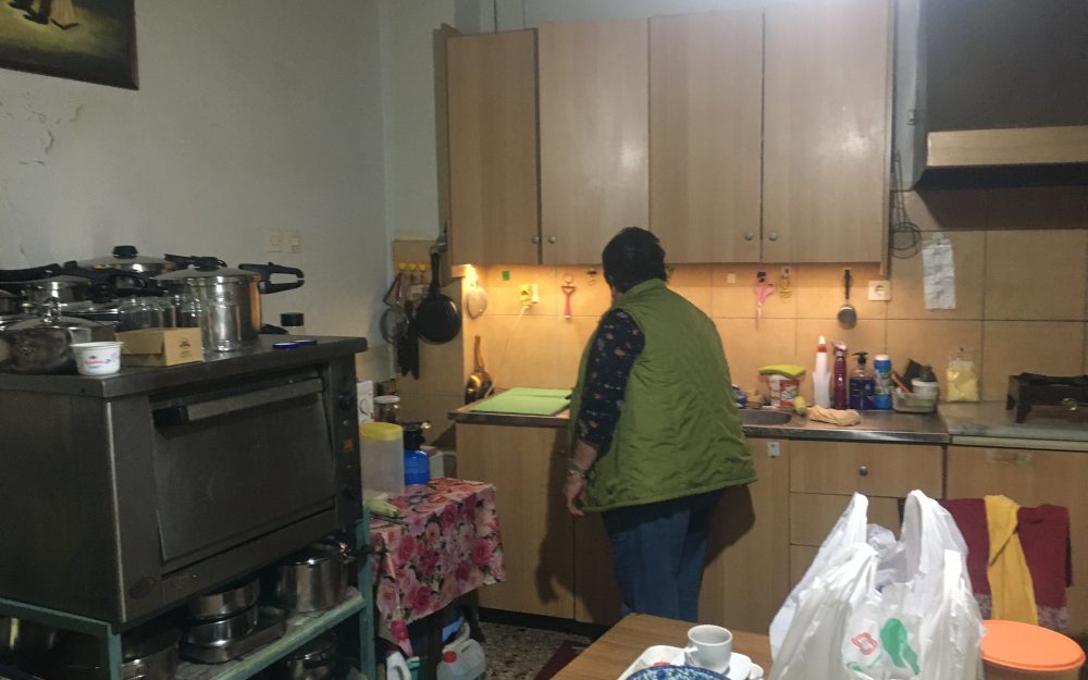 Woman in her kitchen with plastic bag of groceries on kitchen table.