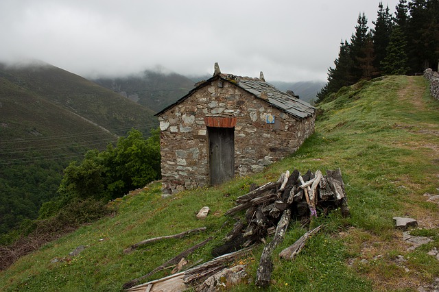 Small stone hut with shingle roof tiles on side of grassy mountain