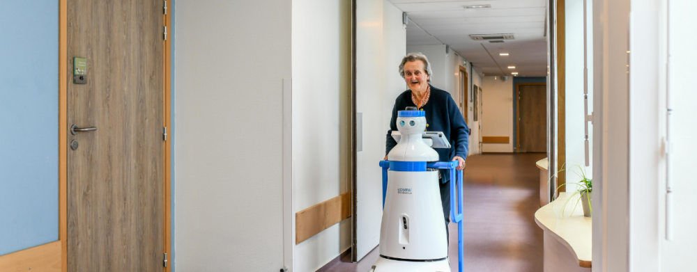 Older woman using Kompaï robot to assist her on her daily walk.