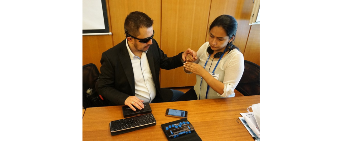 Samuel Valencia (Colombia) is testing a digital solution on his smart phone with a braille line, with the assistance of his female interpreter guide. 