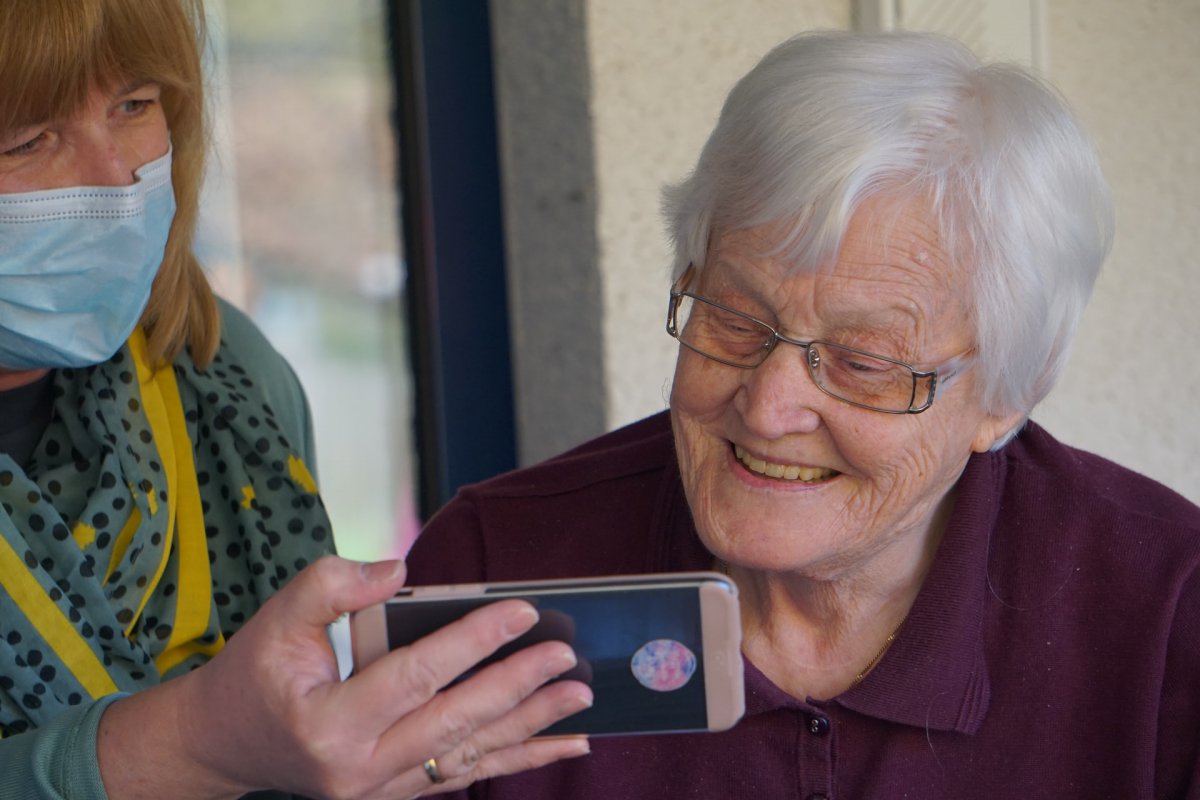 Woman holding a cellphone and showing something on the screen to an elderly woman.